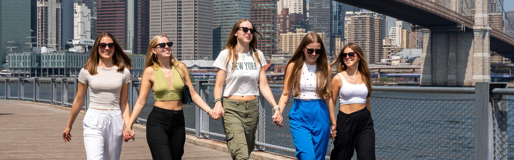 Au pair i USA En grupp au pairer går sida vid sida i Manhattan med Brooklyn Bridge i bakgrunden
