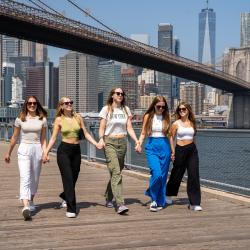 En grupp au pairer går sida vid sida i Manhattan med Brooklyn Bridge i bakgrunden